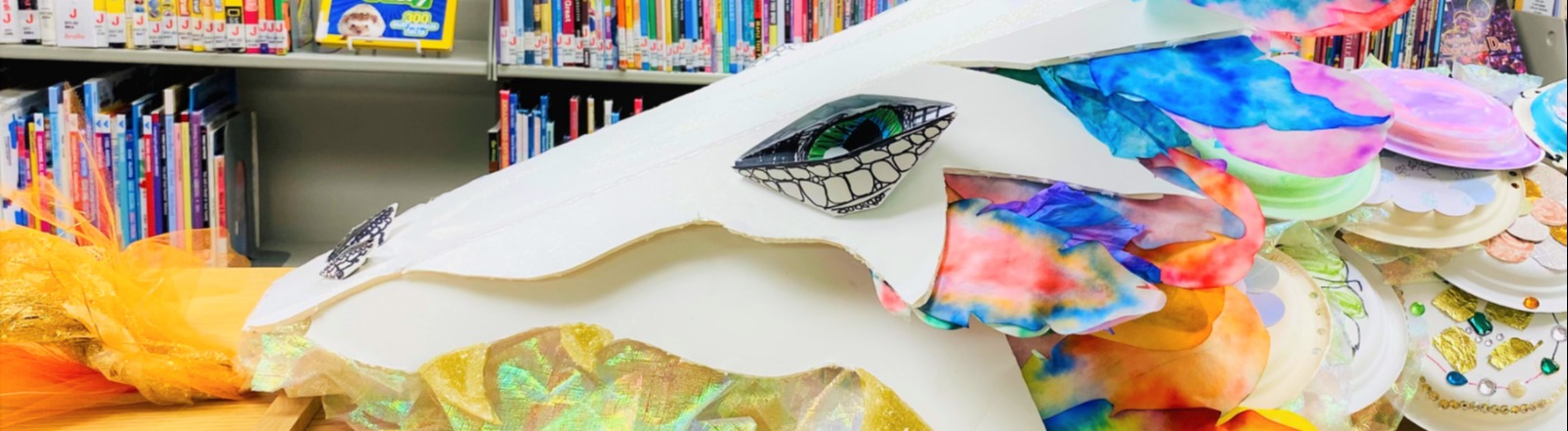Dragon constructed of decorated paper plates amongst bookshelves.
